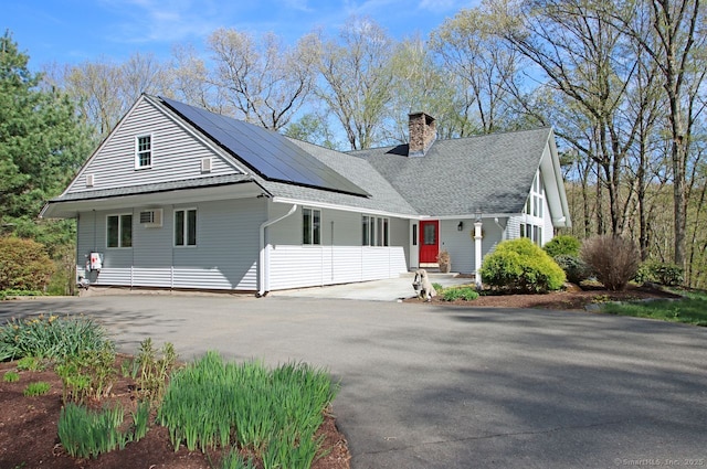 view of front of home with a shingled roof, driveway, a chimney, and solar panels
