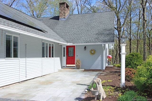 doorway to property with roof mounted solar panels, roof with shingles, and a chimney