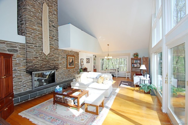 living room featuring a tiled fireplace, high vaulted ceiling, wood-type flooring, and a notable chandelier