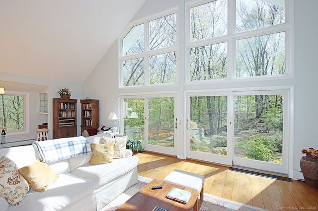 living room with wood-type flooring, high vaulted ceiling, a baseboard heating unit, and a healthy amount of sunlight