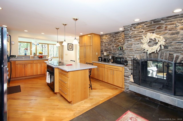kitchen featuring light countertops, a stone fireplace, recessed lighting, light wood-type flooring, and black appliances
