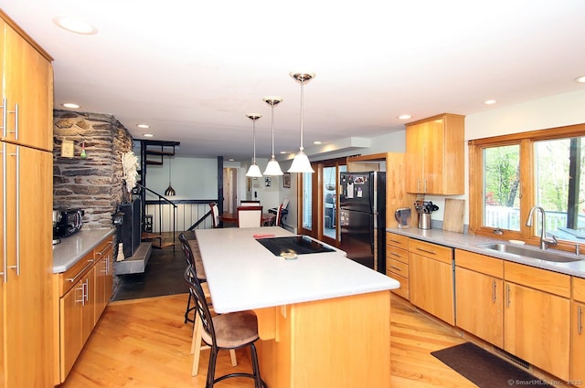 kitchen with freestanding refrigerator, a kitchen island, a kitchen breakfast bar, a sink, and light wood-style flooring