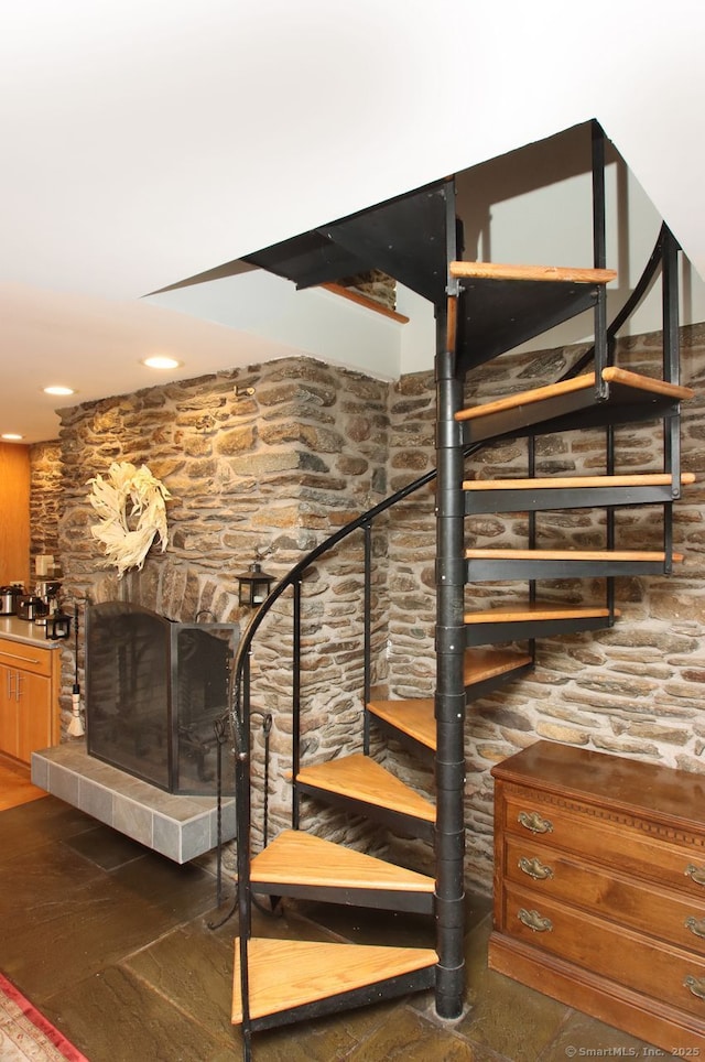 stairs with a fireplace with raised hearth, recessed lighting, and wood finished floors