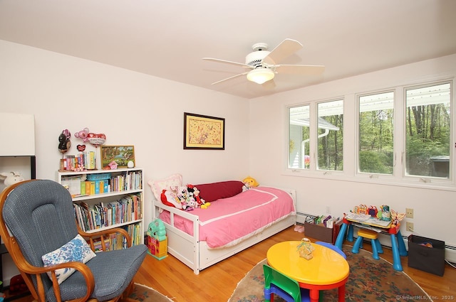 bedroom with ceiling fan, a baseboard heating unit, and wood finished floors