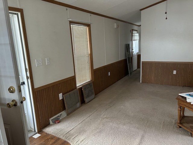 unfurnished room featuring crown molding, wood walls, a wainscoted wall, and carpet flooring