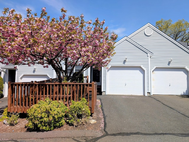 view of property hidden behind natural elements featuring an attached garage and driveway