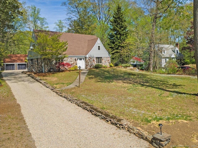 view of front of property featuring stone siding, a front lawn, a garage, and an outdoor structure