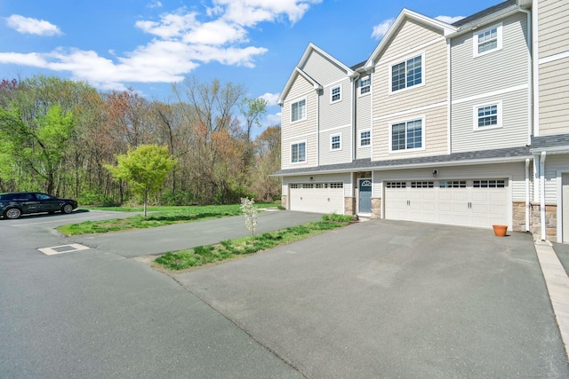 view of front of home with asphalt driveway, an attached garage, and stone siding