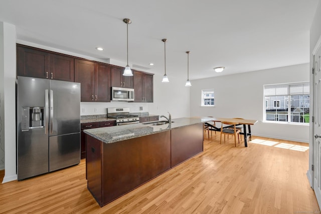 kitchen featuring stainless steel appliances, light wood finished floors, dark brown cabinetry, a sink, and stone countertops