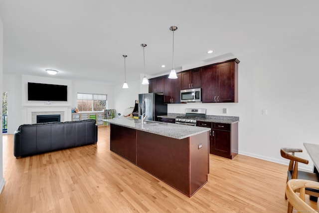 kitchen with appliances with stainless steel finishes, light wood finished floors, pendant lighting, light stone counters, and recessed lighting