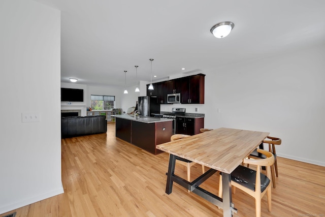 kitchen with appliances with stainless steel finishes, open floor plan, a kitchen island with sink, light wood-style floors, and a fireplace
