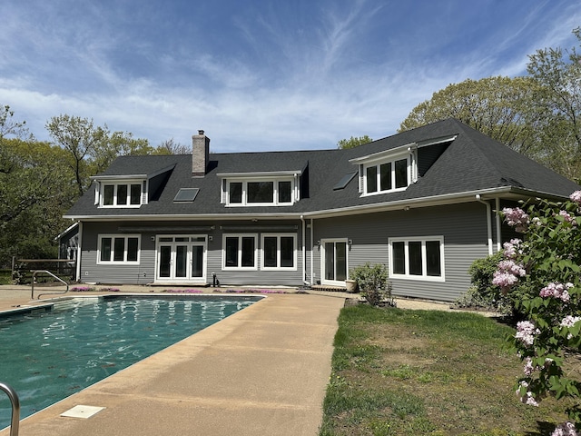 rear view of house featuring roof with shingles, an outdoor pool, a chimney, french doors, and a patio