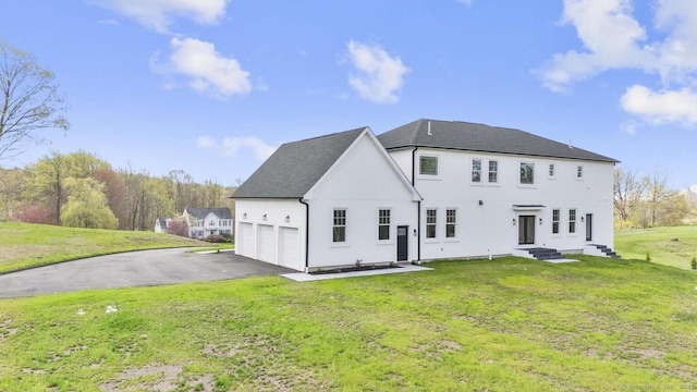 back of property featuring a lawn, driveway, a shingled roof, and stucco siding