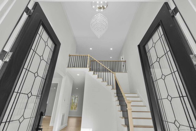 entrance foyer with a high ceiling, an inviting chandelier, recessed lighting, wood finished floors, and stairway