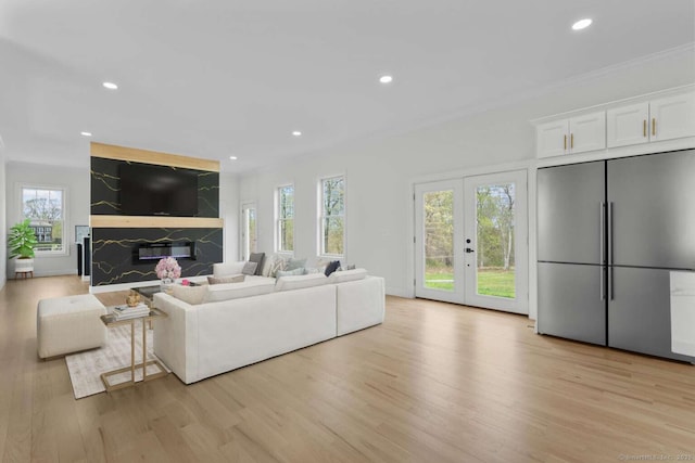 living room with french doors, light wood-style floors, ornamental molding, recessed lighting, and a premium fireplace