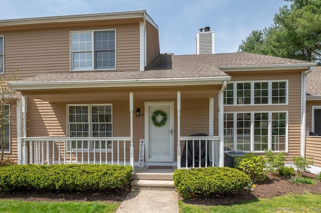 view of front of home with a porch, a chimney, and a shingled roof