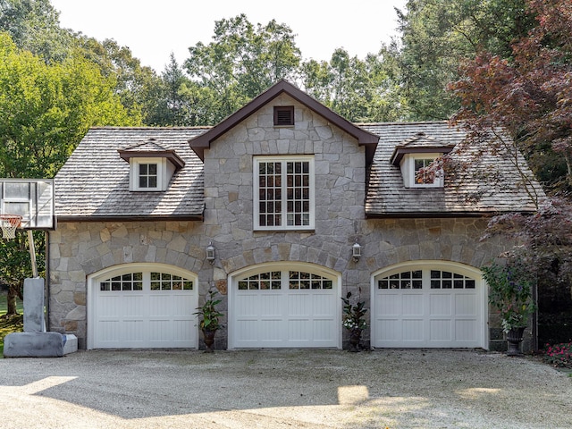 view of front of home with stone siding, an attached garage, and gravel driveway