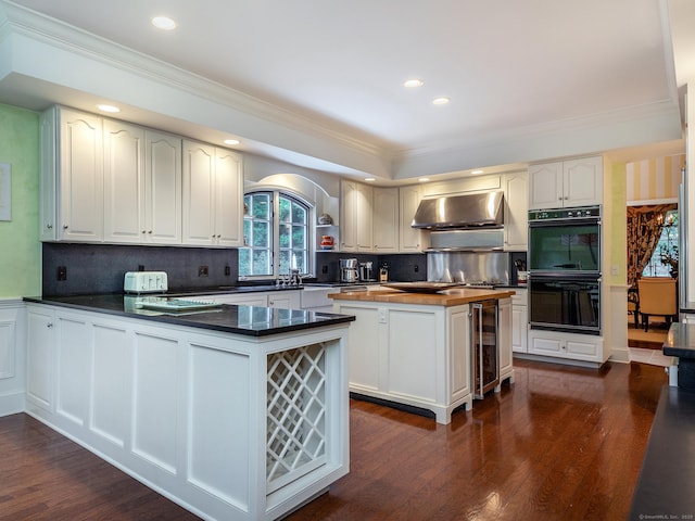 kitchen featuring exhaust hood, wine cooler, crown molding, a peninsula, and dark wood-type flooring