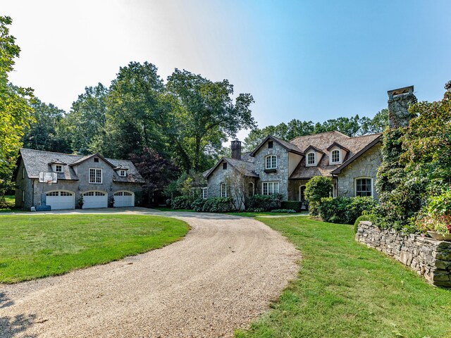 french provincial home with stone siding, curved driveway, an attached garage, and a front lawn