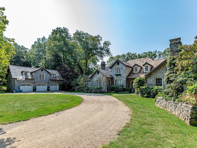 french country inspired facade featuring stone siding, curved driveway, a garage, and a front yard