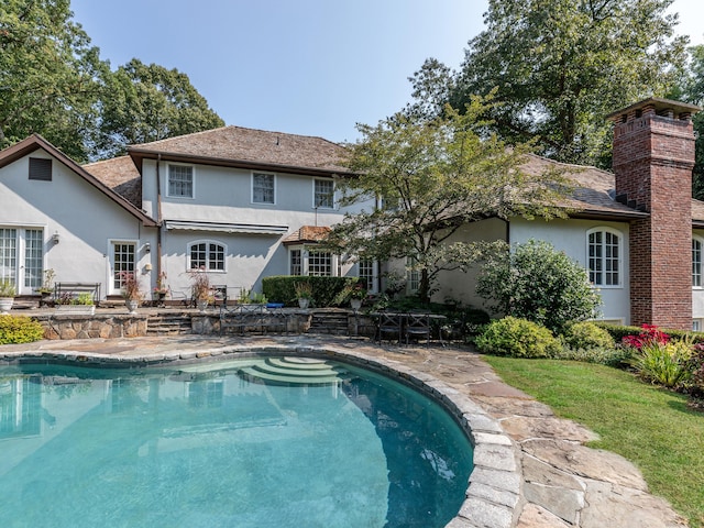 back of property with stucco siding, an outdoor pool, a chimney, and a patio