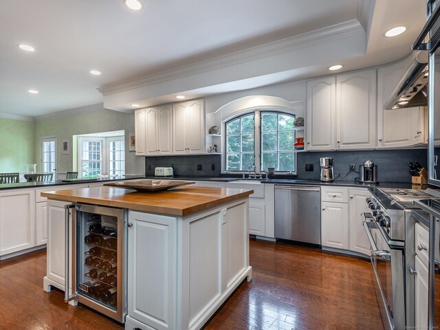 kitchen with appliances with stainless steel finishes, butcher block counters, wine cooler, a kitchen island, and white cabinetry