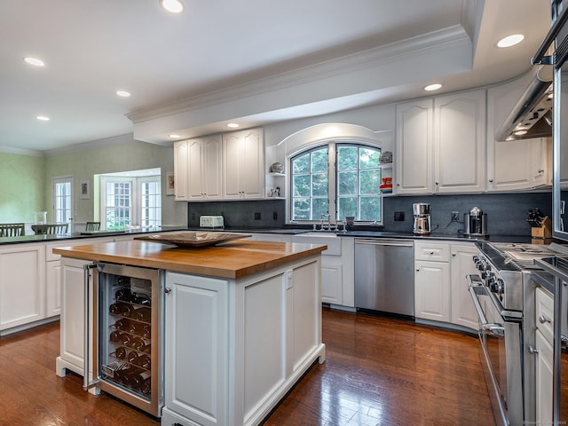 kitchen with stainless steel appliances, butcher block counters, beverage cooler, a center island, and white cabinetry