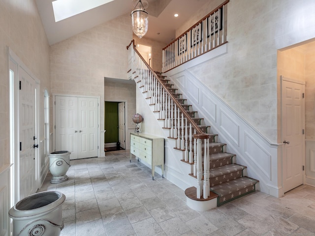 staircase featuring high vaulted ceiling, stone tile floors, a skylight, a decorative wall, and recessed lighting