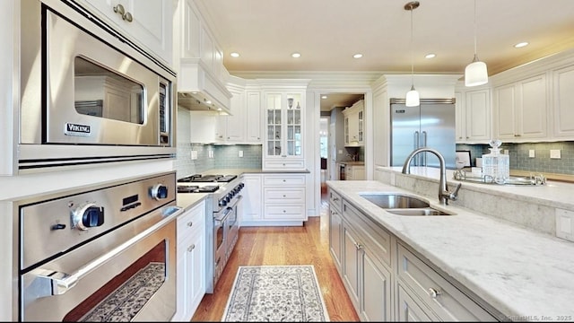 27 Dock Rd, Milford, CT 06460 - kitchen with pendant lighting, a sink, white cabinets, built in appliances, and light wood-style flooring