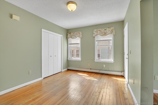 unfurnished bedroom with a closet, hardwood / wood-style floors, baseboards, a textured ceiling, and a baseboard heating unit