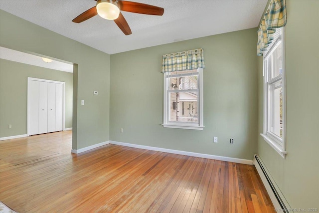 empty room with a ceiling fan, baseboards, a baseboard heating unit, and light wood finished floors