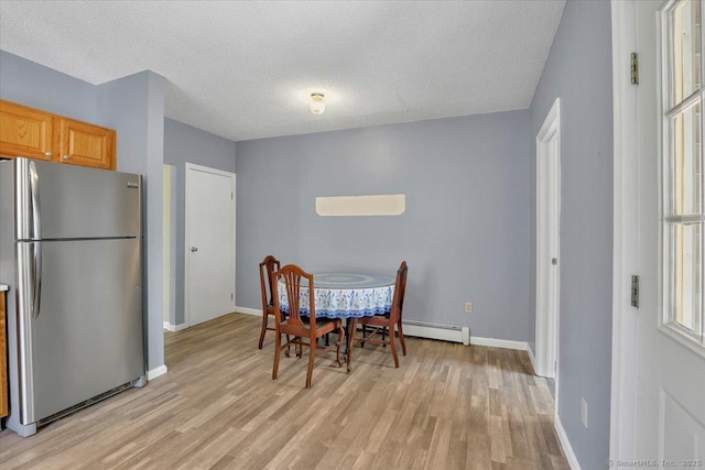 dining room featuring light wood-style floors, baseboards, a baseboard radiator, and a textured ceiling
