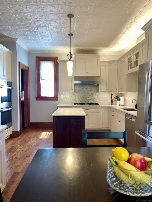 kitchen featuring appliances with stainless steel finishes, a sink, baseboards, under cabinet range hood, and ornamental molding