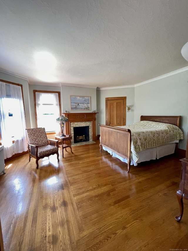 bedroom with crown molding, a textured ceiling, a fireplace with flush hearth, and wood finished floors