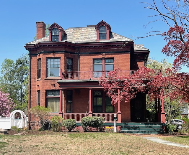 view of front of property featuring fence, a balcony, a front yard, brick siding, and a porch