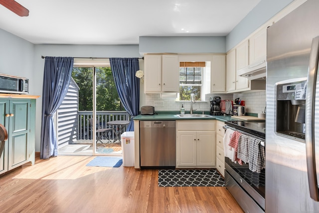 kitchen with a sink, stainless steel appliances, under cabinet range hood, backsplash, and light wood-style floors