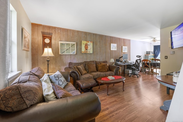 living room featuring wooden walls, a ceiling fan, and wood finished floors