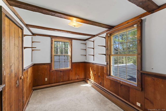 carpeted empty room with plenty of natural light, wood walls, wainscoting, and beamed ceiling