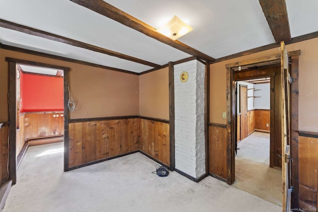 carpeted spare room with a baseboard radiator, wainscoting, wooden walls, and beamed ceiling