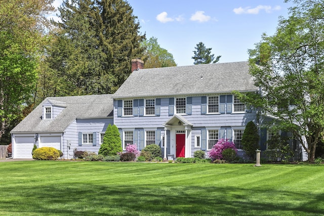 colonial-style house featuring an attached garage, a shingled roof, a front lawn, and a chimney
