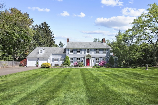 colonial inspired home featuring a front lawn, aphalt driveway, fence, and a chimney