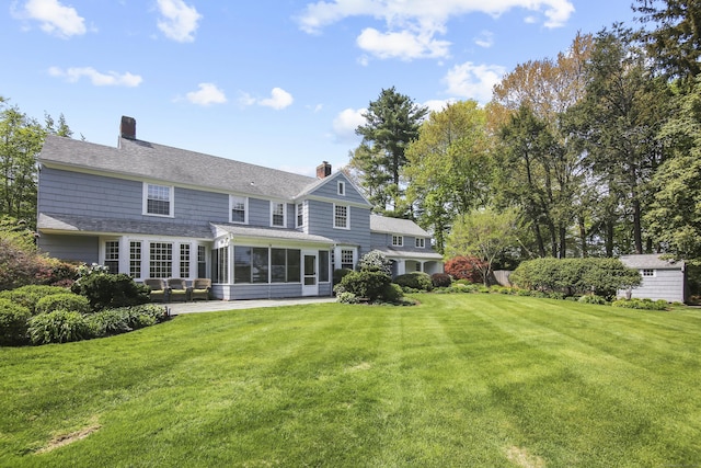 rear view of property with a lawn, a chimney, a sunroom, and roof with shingles