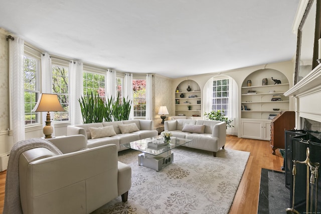 living area featuring a healthy amount of sunlight, built in features, a fireplace, and light wood-type flooring