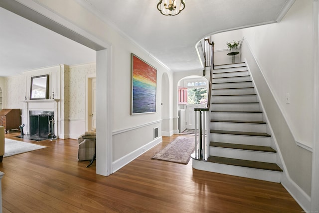 staircase with visible vents, crown molding, arched walkways, a high end fireplace, and wood finished floors