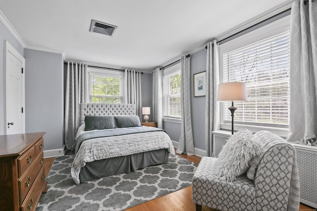 bedroom with crown molding, baseboards, wood finished floors, and visible vents