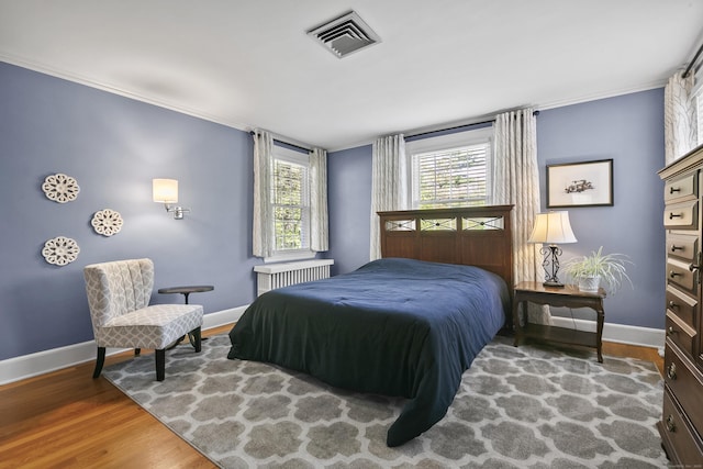 bedroom with radiator heating unit, baseboards, wood finished floors, and visible vents