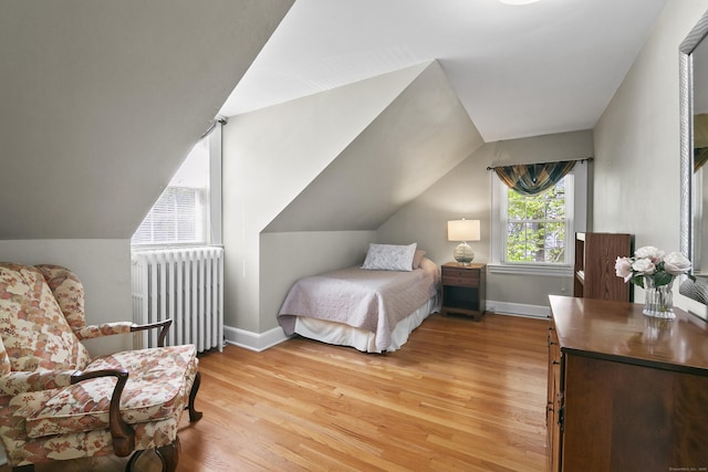 bedroom with baseboards, light wood-style flooring, radiator, and vaulted ceiling