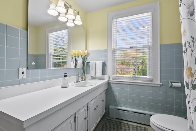 bathroom with plenty of natural light, a baseboard radiator, wainscoting, and tile walls