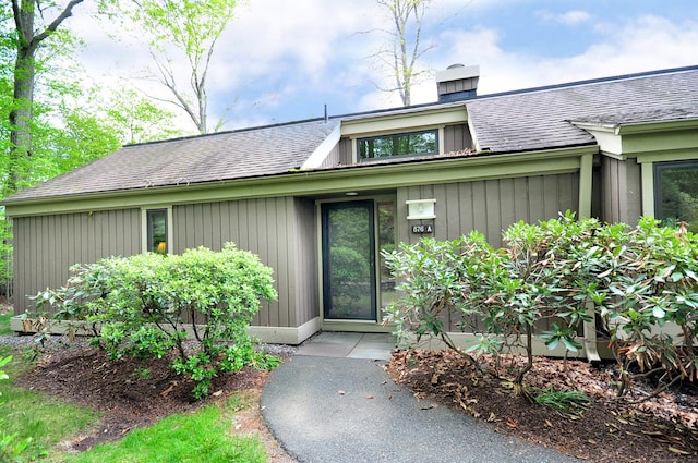 doorway to property with a shingled roof and a chimney