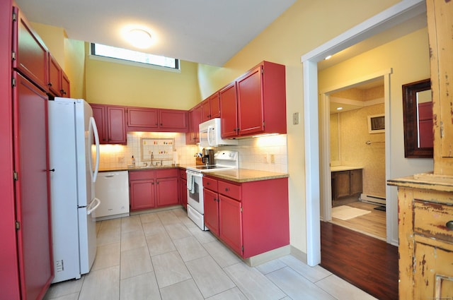 kitchen with white appliances, red cabinetry, a sink, baseboard heating, and a towering ceiling